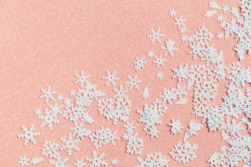 Light pink background with glitter and sequins in the form of white snowflakes and Christmas trees. Winter soft texture for creative projects and advertising design