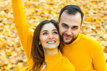 Couple dressed in yellow turtlenecks hugging on a background of autumn leaves