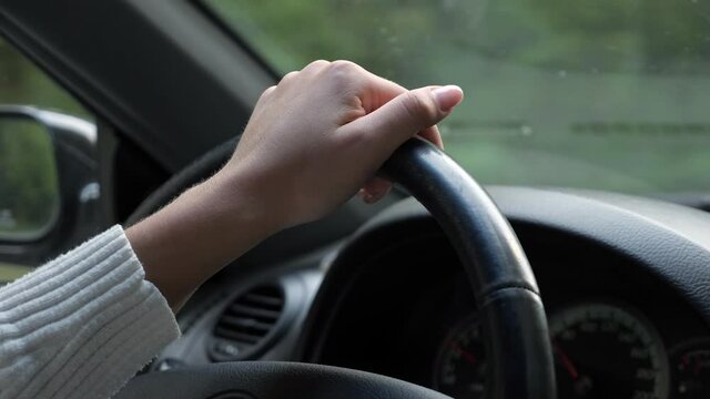 Manicured lady in white pullover hand on black leather steering wheel at designed dashboard with speedometer in new riding automobile closeup