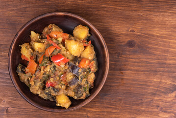 Traditional Italian vegetable stew with potatoes, eggplant, tomatoes and peppers in a rustic earthenware plate on a woody background, copy space - Neapolitan style cianfotta.