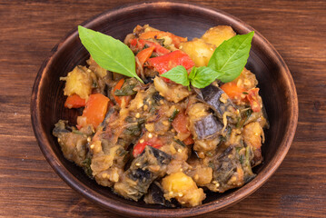 Italian vegetable stew with potatoes, eggplants, tomatoes, pepper in a rustic clay plate, decorated with fresh basil leaves on a woody background - Ciambotta, cianfotta in Neapolitan style.