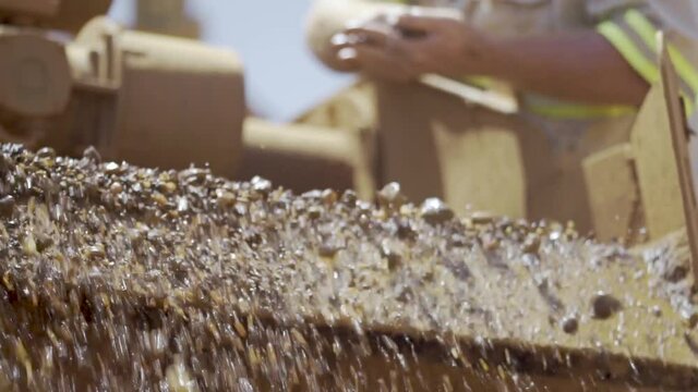 Miner checks gravity separator of pulsating mineral jig catchment tray as waste material exits machine on open ground diamond mine. Close up.