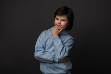 Photo of Pensive boy 10-12 years old standing with hand raised on chin. Studio shot, gray background