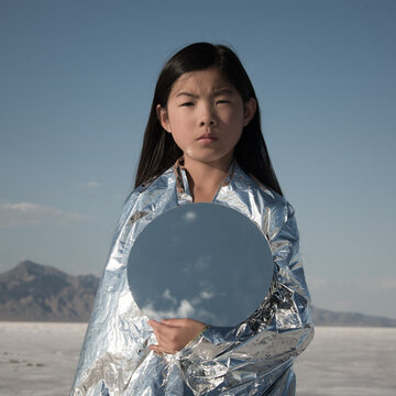 Girl in silver holding a round mirror reflecting the blue sky  in bonneville salt flats, utah