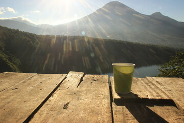 a warm drink on a wooden table against a scenic backdrop and flares of sunshine. enjoy morning coffee at the top of the mountain
