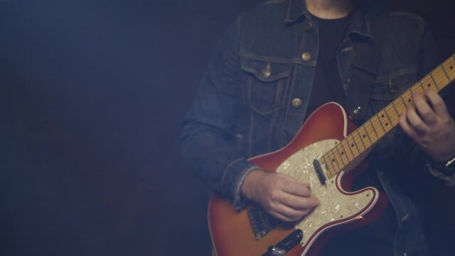 This is a close up shot of a fashionable man playing electric guitar on stage. This is a hand held shot in a contemporary setting with lots of energy.