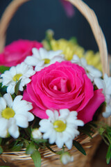 Gift bouquet of flowers in a wicker basket with a handle on a dark background.