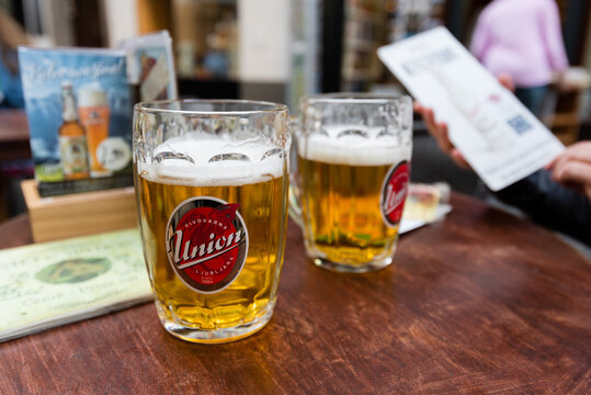 Ljubljana, Slovenia - 09 03 2017: Two glasses with beer from the brewery "Pivovarna Union" standing on wooden table while one person is looking at the menu in blurred background