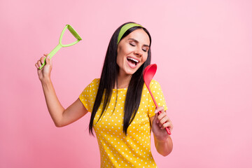 Photo of joyful young housemaid wear yellow dotted t-shirt pin-up sing spoon isolated on pink color background
