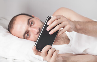 Surprised man using smartphone in bed.