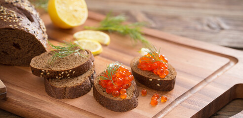 red caviar with bread, dill and lemon on  wooden board