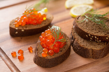 red caviar with black bread, dill and lemon on  wooden board