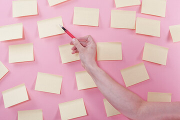 Hand holding pen, pointing at yellow sticky notes on pink background.