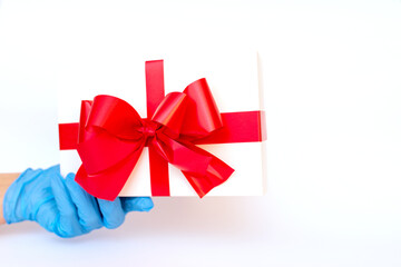 Holiday gift.Hand wearing meidical gloves holding gift box with red ribbon.white background.