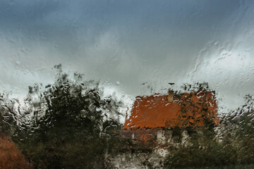 Drops on glass in rainy day.Rain outside window in the countryside. Texture of raindrops, wet glass.Rainy window background.View through the window with stormy sky. Staying at home. Weather changes.