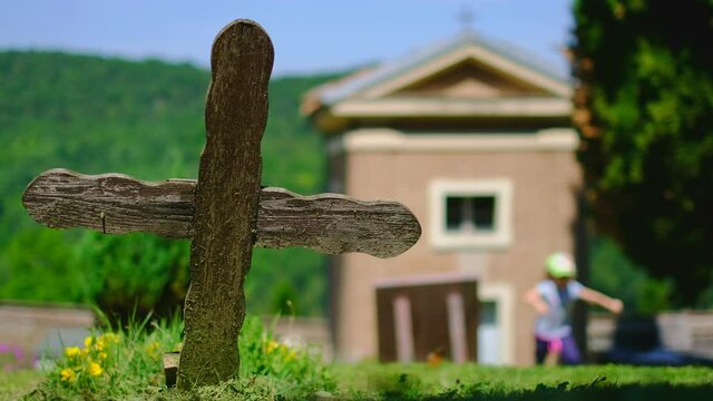old wooden cross in cemetery with small church on sunny day with little girl running in background
