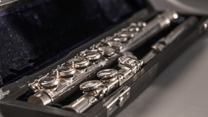 Silver metal flute disassembled in a black case with blue velvet illuminated by the sun