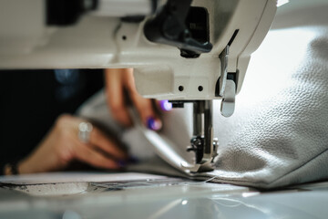 Closeup of female hands sewing gray leather on a machine