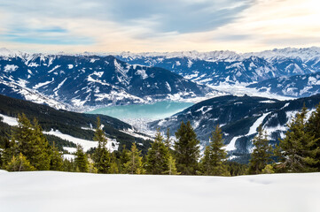 Zell am See and Schmitten town at Zeller lake in winter. View from Schmittenhohe mountain, snowy ski resort slope in the Alps mountains, Austria. Stunning landscape, snow and sunset sky near Kaprun