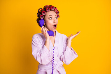 Portrait of lovely amazed stunned cheerful woman wearing curlers talking on phone having fun isolated bright yellow color background