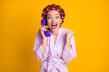 Portrait of attractive cheerful ecstatic woman wearing curlers talking on phone having fun isolated vivid yellow color background