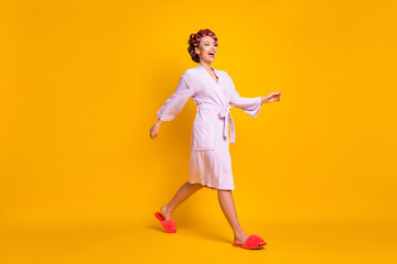 Full length body size profile side view of nice cheerful housemaid wearing curlers walking isolated over bright yellow color background