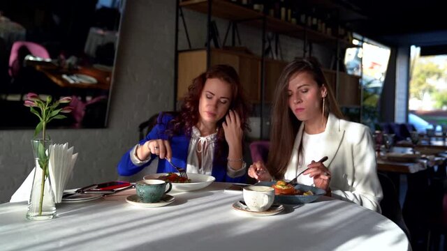 two young colleagues women are dining together in restaurant, ladies are sitting at table and eating