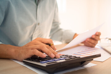 Business people sit at the desk using a calculator to calculate the profit-loss figures shown in the document graph. Concept of using calculator