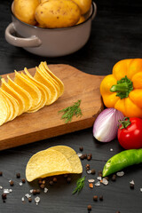 Potato chips and vegetables in composition on black background