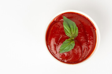 Tomato paste in bawl and basil leaf on white background
