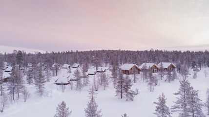 Visit Lapland Holidays. Aerial drone panorama shot of the forest covered in snow winter and the village inside the Arctic Circle. Lapland, Finland. Winter sunrise. Igloos and cabins covered with snow