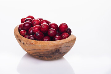 Fresh raw organic cranberry in wooden bowl plate on white background with berries next to it. Space for text.