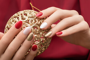 Christmas nail design. Female hands with red and golden manicure. Female hold golden xmas toy orb....