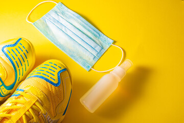 Top view of fitness shoes, surgical mask, and hydro alcoholic gel on a yellow background