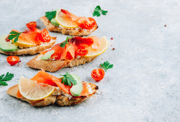 Smoked salmon sandwich with cream cheese, lemon, avoado and tomato on gray background. Selective focus