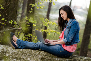 Junge Frau mit Laptop auf einem Baumstamm