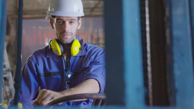 Concentrated forklift caucasian driver operating machine and holding hand on steering wheel  radio comminication operate teamwork with transportation of goods cargo in factory warehouse workshop.