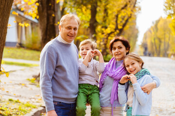 Fototapeta premium A Family of four, mom, dad, son and daughter showing heart with hands enjoying sunny weather golden leaves in autumn park