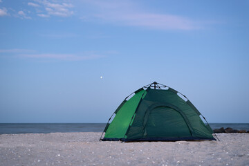 Green tent against blue sky and sea background. Camping on beach. Evening