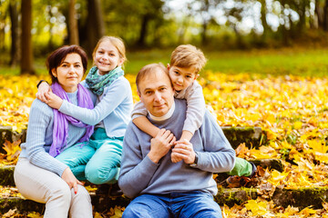 Naklejka na ściany i meble Happy family in the park for a walk in the summer, in the fall. Mother, father and two children walking on nature. Parents and children smile, laugh, play in the afternoon.