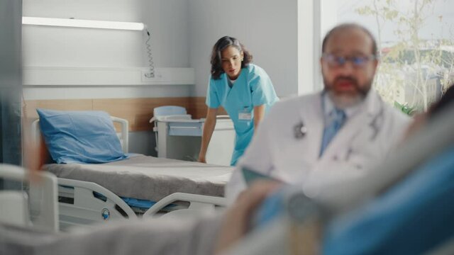 Hospital Ward: Resting on Medical Bed Female Patient Listens to Experienced Latin Physician who Uses Digital Tablet Computer to Show, Explains Analysis Results. In Background Nurse Working