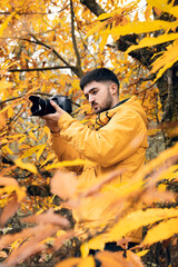 young student boy making a photo among yellow leaves in the forest with yellow autumnal coat