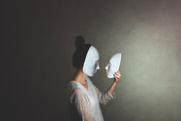 woman with mask looks at another mask of herself, concept of introspection