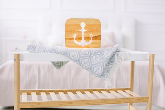 Wooden lapms and decor details at home interior. Stylish wooden hand made lamp with anchor cut out picture, on little coffee table, standing in light home bedroom