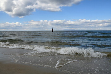 View of the Polish sea with some land in the distance and some reeds or shrubs growing next to the sandy coast of the reservoir seen on a cloudy yet warm day on a Polish countryside next to a resort