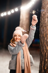 Christmas sparkles in hands. Cheerful young woman celebrating holding sparkles in the winter forest. Festive garland lights. Christmas, new year.	