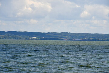 View of the Polish sea with some land in the distance and some reeds or shrubs growing next to the sandy coast of the reservoir seen on a cloudy yet warm day on a Polish countryside next to a resort