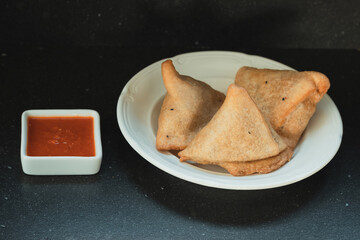 Samosas on a wooden table served with hot red sauce on white porcelain