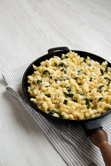 Homemade Spinach Mac and Cheese in a cast-iron pan on a white wooden surface, side view. Copy space.
