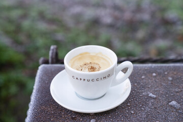 Frosty morning with coffee outside. White cup of cappuccino on a frozen rustic metal pattern. Freshly fall winter background.